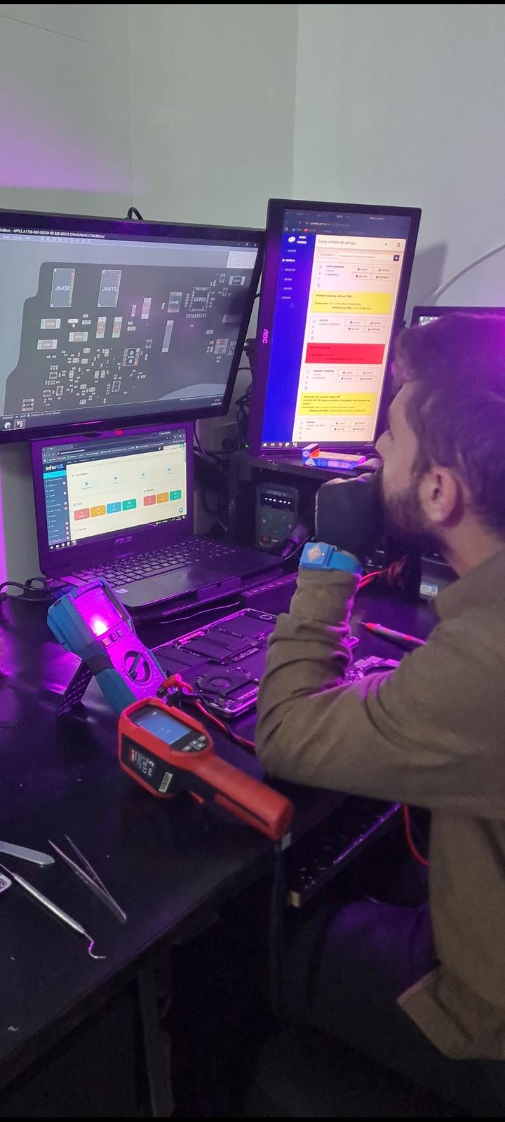 Técnico da Sigma analisando o esquema elétrico de um MacBook com multímetro e câmera térmica
